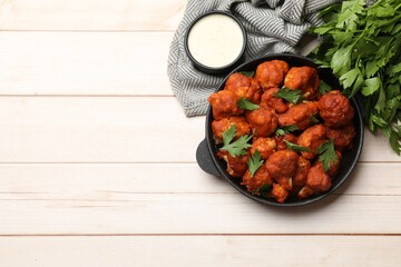 Baked cauliflower buffalo wings in baking dish, sauce and parsley on wooden table, top view. Space for text