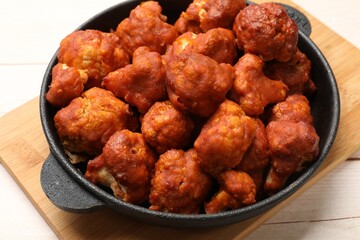 Baked cauliflower buffalo wings in baking dish on wooden table, closeup