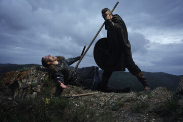 Fierce fight between two medieval barbarian warriors against dramatic landscape