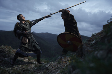 Fierce fight between two medieval barbarian warriors against dramatic landscape
