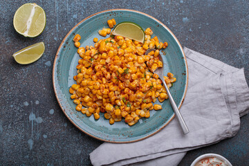 Plate of esquites, a popular mexican street food dish, are served with lime wedges and sour cream with chili powder