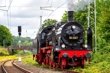 Historic steam locomotive on the railroad line between Bochum-Dahlhausen and Wetter in the idyllic Ruhr Valley, Germany. Black and red powerful engine with attached coal and water tender.