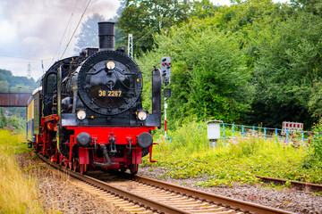 Historic steam train in a curve on the railroad line between Bochum-Dahlhausen and Wetter-Wengern in the idyllic Ruhr Valley, Germany. Nostalgic steam locomotive with a train of old passenger cars.