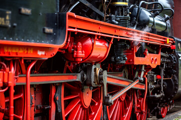 Large cast-iron flywheels from a functioning historic German steam locomotive. Red painted spokes and connecting rods and oiled bare steel. Railroad technology from bygone times that still inspires.