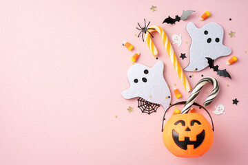 Playful Halloween setup with ghosts, candy, pumpkin bucket, bats, spider, and colorful decor on a pink background