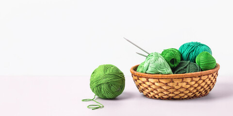 Green knitting balls in a basket with knitting needles on gray background. Set for the hobby of knitting warm clothes or toys. Concept needlework