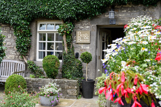 Charming bed and breakfast exterior with lush greenery, colorful flowers, and a welcoming wooden bench.