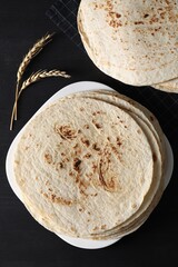 Many tasty homemade tortillas on black wooden table, top view