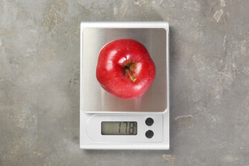 Kitchen scale with apple on grey textured table, top view