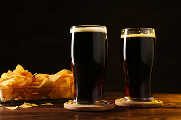 Glasses of beer and potato chips on wooden table
