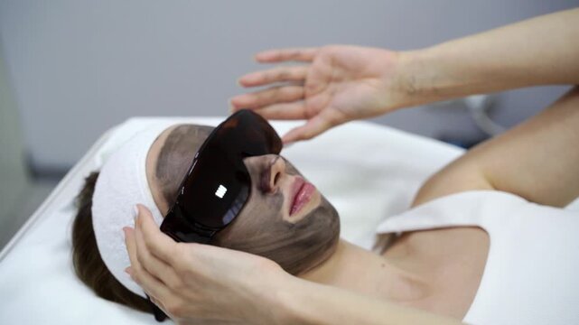 Doctor prepare to laser facial treatment. A woman undergoes a rejuvenating peel with a carbon mask, promoting skincare and reducing pigmented lesions. Female face cosmetic. Beauty aps