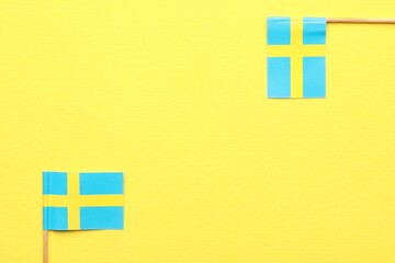Obraz premium Small paper flags of Sweden on yellow background, top view. Space for text