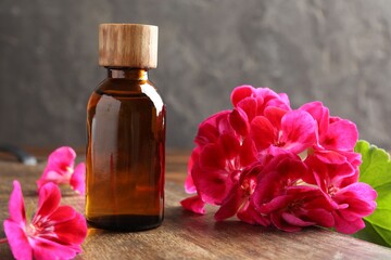 Geranium essential oil in bottle and beautiful flowers on wooden table