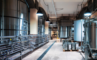 Spacious modern brewery interior featuring large stainless steel tanks, intricate piping and atmospheric lighting, reflecting high-quality beer production standards.