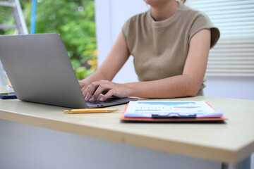 Fototapeta premium Successful Asian businesswoman sitting at desk working using laptop computer in office. Business and people concept. Businesswoman using laptop computer and working with documents.