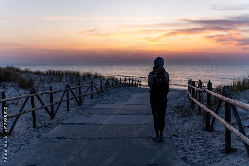 Sticker Person standing on a beach pathway at sunset, looking at the ocean