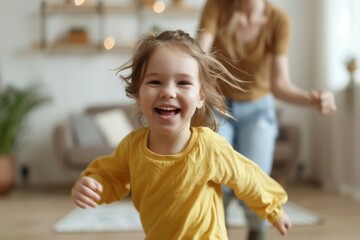 A young girl is running in a yellow shirt and smiling. She is accompanied by a woman who is also smiling. The scene is lively and joyful, with the two women enjoying their time together
