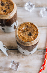 Trendy drink, Fluffy Coke, is a refreshing beverage made with cola, ice, and whipped marshmallows. A refreshing cola cocktail in two glass cups shaped like tin cans. Ice cubes and red paper straws.