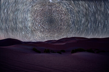 Silhouette of a man pointing to Polaris - North Star light trails over the dunes in Abu Dhabi