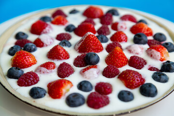 In a plate with whipped cream ripe berries strawberries raspberries and blueberries on a blue background