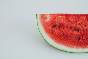 side view of a slice of a huge juicy watermelon with black seeds on a white background