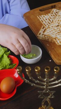A Jewish woman in blue at a laid Pesach Seder table dips karpas in salt water