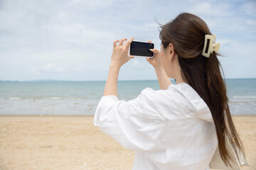 Asian woman using her phone taking photo on the beach