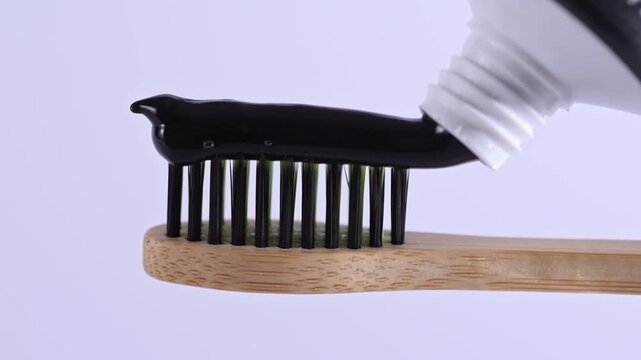 Putting charcoal toothpaste on bamboo toothbrush on white background. Applying a swatch of black charcoal whitening toothpaste on brush.