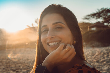 Beautiful brunette girl headshot close-up on a beautiful smiley face on a beach with sun rays coming in by sunset