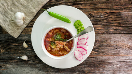 Delicious homemade beef tripe soup served with fresh green chilies and sliced radishes on rustic wooden table view from above