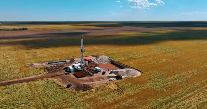 Flying away from the gas producing site located in the vast field. Shadows from clouds are on the ground.
