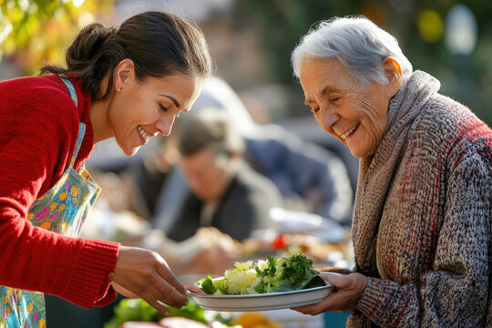 Smiling young volunteer serving a plate of food to a senior woman outdoors