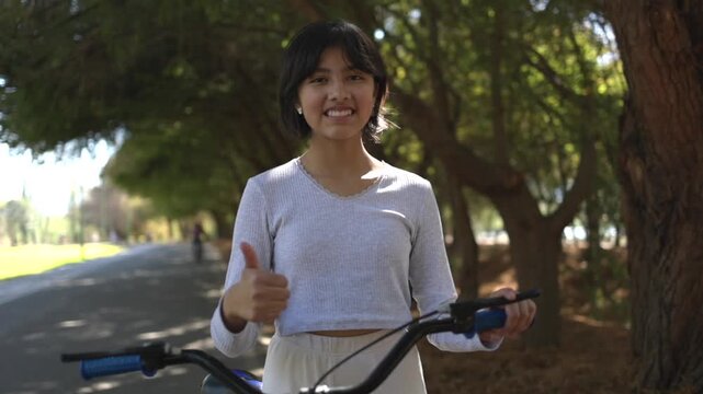 Portrait of a Mexican teenager posing and smiling  with a bicycle outdoors thumbs up