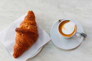 Cup of hot cappuccino coffee and fresh french croissant on a table. Top view