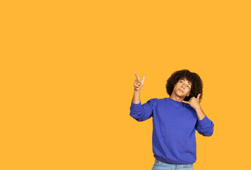 A young guy with curly hair stands against a vibrant yellow background, playfully gesturing with...