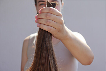 A hand holds a freshly cut bundle of long, brown hair against a plain background. The hair appears...