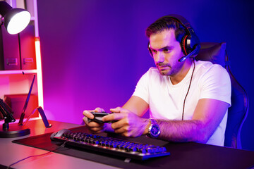 Smart gaming streamer talking with team member players with joystick to control game, mic for communicate with others on streaming live on social media at digital neon lighting studio room. Surmise.