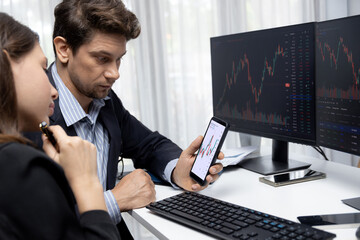 Focusing on phone with discussing dynamic stock market in two business traders online website compare with pc screens in real time currency rate investment on risk data at modern office. Postulate.