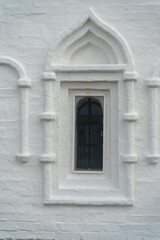 A window in the white wall of an ancient temple or building. A window on a white brick wall.