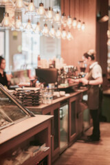 Coffee shop counter with baristas serving customers, stacks of packaged goods. Blurred background