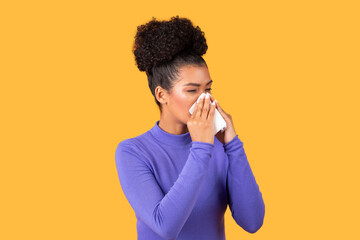 A young woman wearing a purple long sleeve top is using a tissue to sneeze, showing an expression...