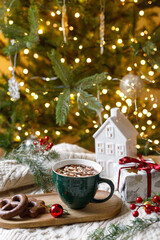 Warm cup of cocoa with marshmallows and chocolate cookies, christmas ornaments and gift on cozy...