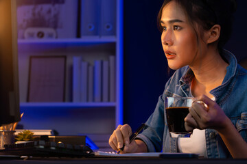 Thinking young beautiful Asian creative woman analyzing profit while drinking coffee, comparing on email sending business market report, writing on notebook for memo at neon light at night. Stratagem.