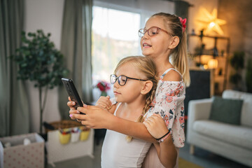 Young girls child hug and use mobile phone, play together at home