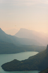 Two paragliders in the air fly over the mountains at summer sunrise.