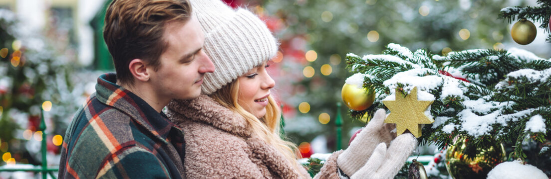 Cozy atmosphere of outdoor christmas market. Festive mood, holiday spirit. Young beautiful loving couple drinking homemade hot tea or mulled wine from terms bottle. Enjoying winter vacations banner 