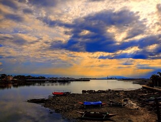 Panorama na port rybacki i piękny zachód słońca. Kolorowe łodzie rybackie stoją przy brzegu. Krajobraz roztacza się na rzekę, błękitne niebo i góry w oddali (Manila, Filipiny) © Adam