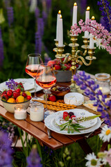 Perfect surprise date for loving couple, private wedding, romantic marriage proposal. Summer, sunset, golden hour. Appetisers. Beautiful elegant outdoor arrangement in meadow with purple blue lupins