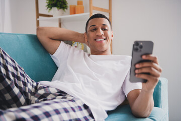 Photo of attractive funny guy nightwear pajama enjoying weekend couch commincating instagram...