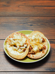 Meal with two pita bread with chopped cooked chicken fillet and melted cheese on a green plate and wooden table. Pizza style dish. Quick lunch.